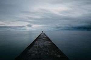 Pier into a calm sea that almost reaches the horizon, with a person standing on the end