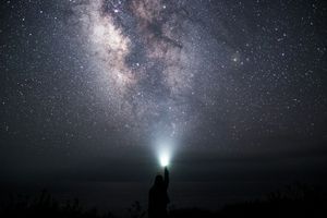 Milky way with a person holding a torch upwards as if the stars are coming out of it